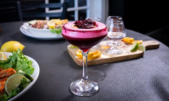 Meals on a black-covered table, with a hibiscus cocktail in the forefront