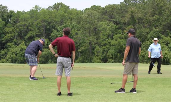 Four men at the green, with one putting, during a charity golf tournament