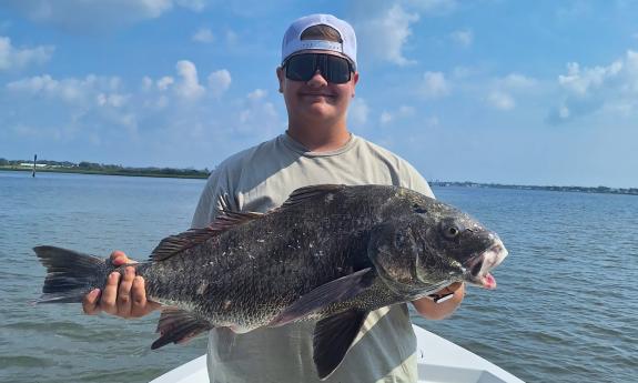 A guest holding a black drum fish
