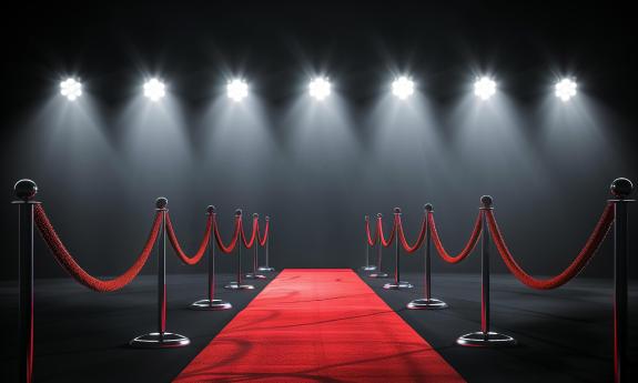 A red carpet, with velvet ropes on the side, under a row of spotlights