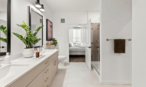 This bath has two sinks, a walk-in shower, and a door to the bedroom