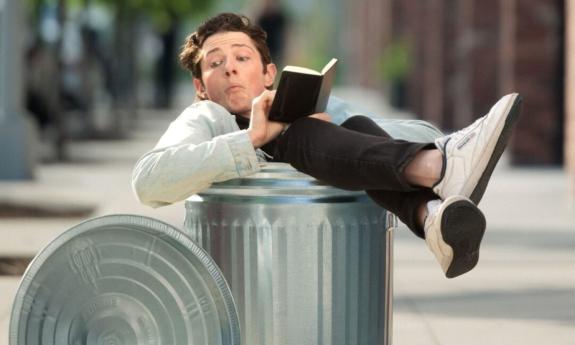 Erik Scott sits in a trashcan while reading a book. 