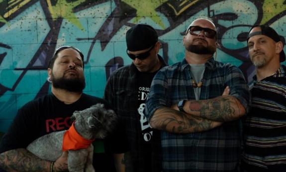 The bandmates of Floridaze strike a pose against a green, graffiti-covered wall. 