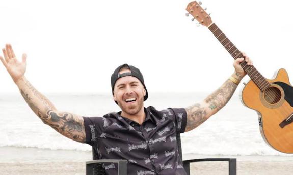 Musician Kyle Smith, holding his acoustic guitar, looking exuberant at the beach