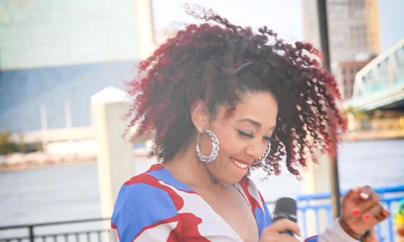 Singer and dancer Awilda Quezada, smiling and holding the mic at an outside venue