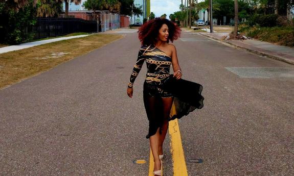 Awilda Quezada, in a flowy one-shoulder dress, walking down the center of the road