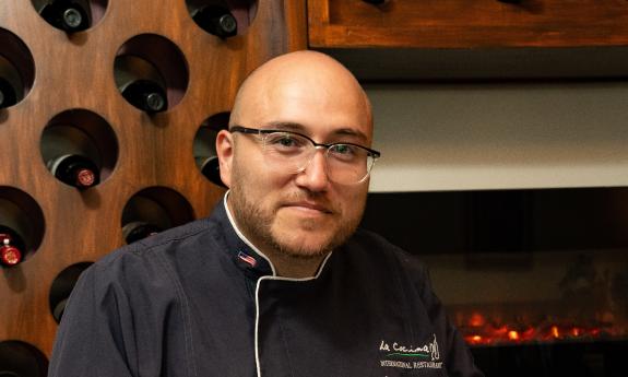 A male chef from La Cocina standing nect to a wine display