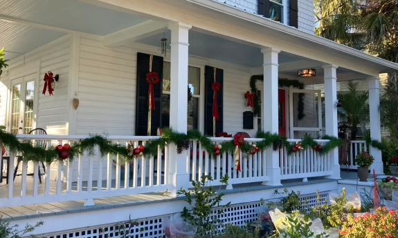 A porch on a large white 1800s home decorated for Christmas