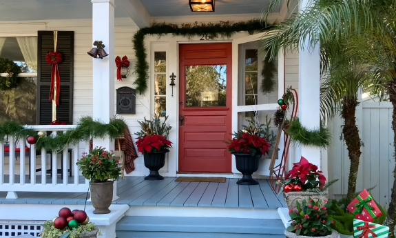 A white porch with a red door decorated for Christmas