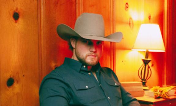 Songwriter Braden Jamison in cowboy hat, sitting inside wood-paneled room
