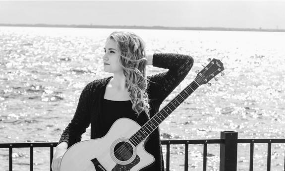 Songwriter Cassidy Lee with guitar next to the water