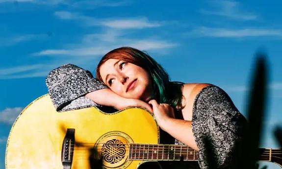 Singer-songwriter Lauren Mullinax leaning on her guitar as she smiles, dreamily