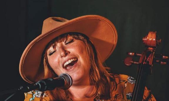 Singer-songwriter Lauren Mullinax in a brim hat, singing in front of a mic