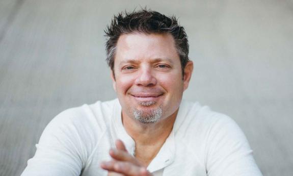 Songwriter Rodney Clawson, smiling, sitting in front of a white wall