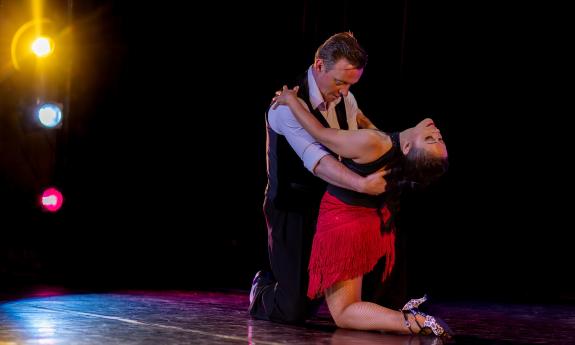 Two dancers on a dark stage with spotlights in a floor pose