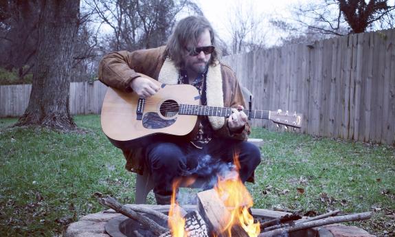 James McNair, singer and songwriter, playing his guitar in his backyard near a fire pit