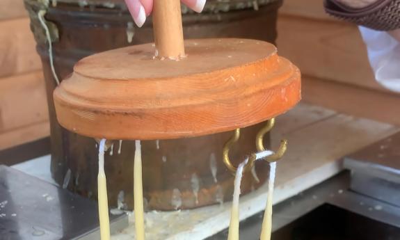 Candles hung by their wicks being dipped in beeswax