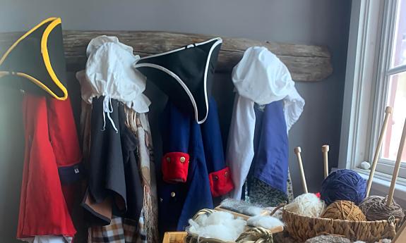 Colonial clothing hanging from pegs with balls of yarn on a table in front