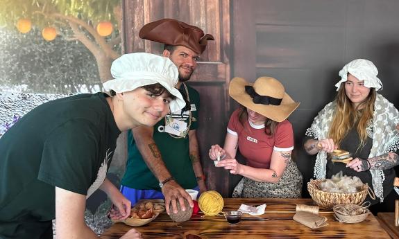 Four people learning to card wool and dye yarn for colonial clothing