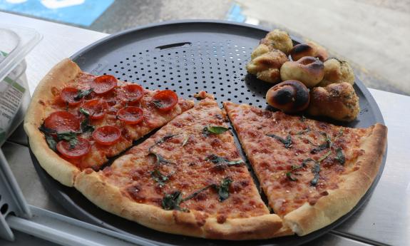 Three slices of different pizza and a small pile of garlic knots on a black pizza pan