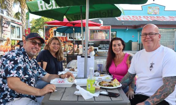 Four people enjoying their food of choice at an outdoor table at Global Bites food truck park