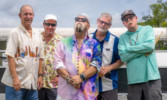 Five band members, standing together outside on a sunny day