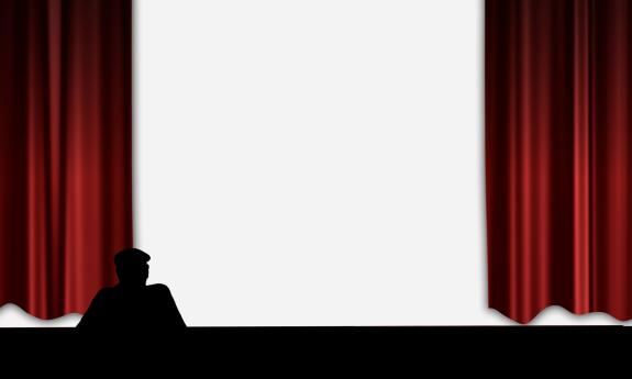 A stage, with red curtains on the edge, and a man in silhuette in the front