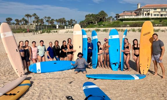Ladies and surf boards, and two instructors, lined up on the beach for a surfing lesson