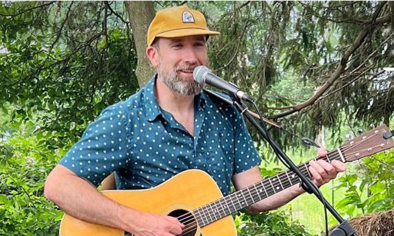 Musician Dave Schottland playing guitar in front of a microphone, outside.