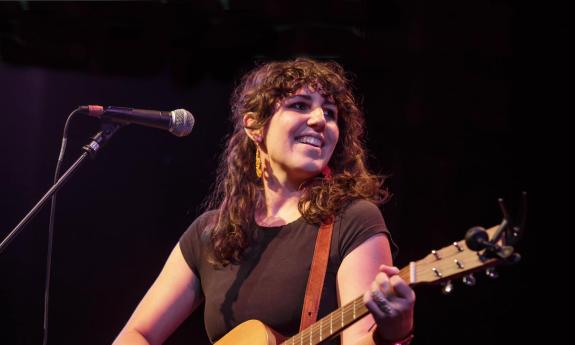 Miriam Morelli on stage, smiling, with her guitar, at night
