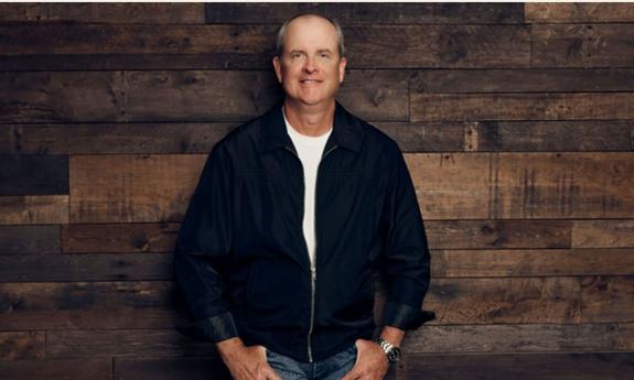 Songwriter Monty Criswell standing in front of a brown wood wall