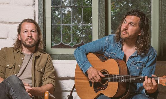 Teskey Brothers sitting in front of a white house, one with a guitar