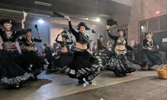 Dancers dressed in long black skirts, cropped tops, and tricorner hats