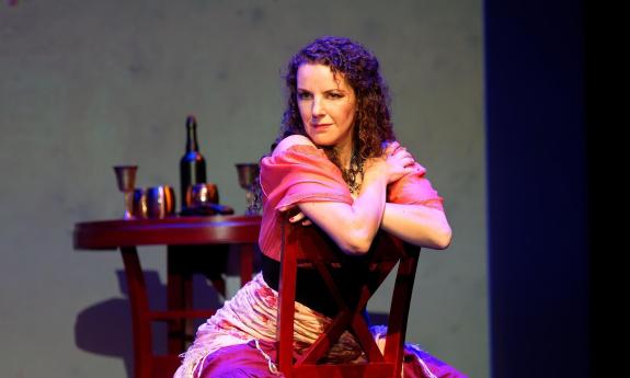A woman, Sarah Nordin, straddles a chair and faces the audience in a scene from Carmen