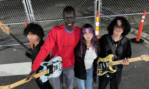 Four musicians of Doubleside standing outside near a chainlink fence