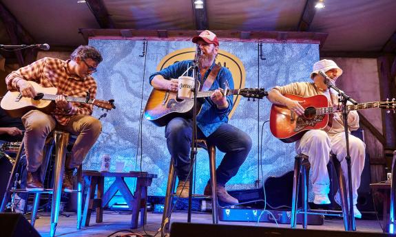 Three musicians/songwriters on stage, with one taking the lead singing his song