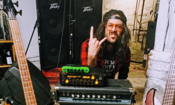 A musician at his mixer, with hat backwards, tongue out, and showing the sign of the horns