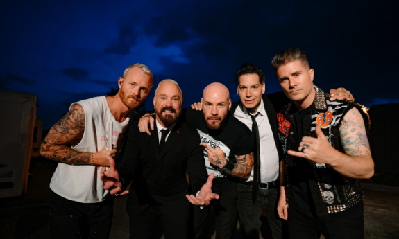 The members of Goldfinger, dressed in black and white, pose together against a dark blue, cloud-filled backdrop.