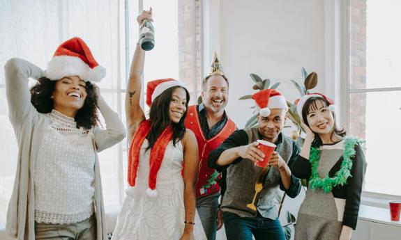 Five people, with festive seasonal hats and champagne celebrate winter holidays