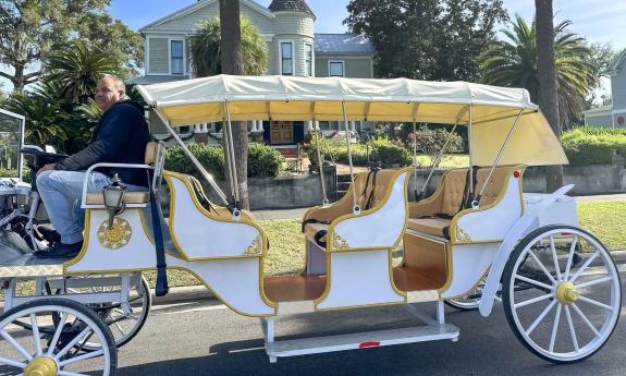 An electric vehicle designed as a horseless carriage replica, with the driver up front