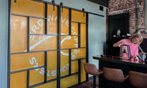 Owner, Jared Bastin, pouring a coffee in front of a wave door