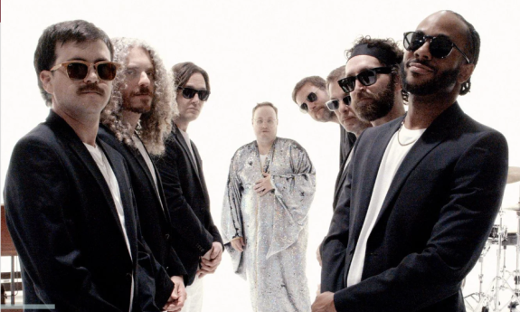 Bandmates from St. Paul & The Broken Bones wear dark clothing and pose in front of a white backdrop.