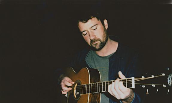 Jordan Tice with his guitar on a dark stage