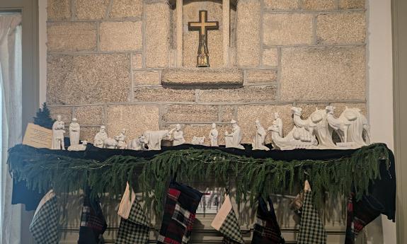 A white many-figured nativity displayed across a mantle trimmed in evergreens