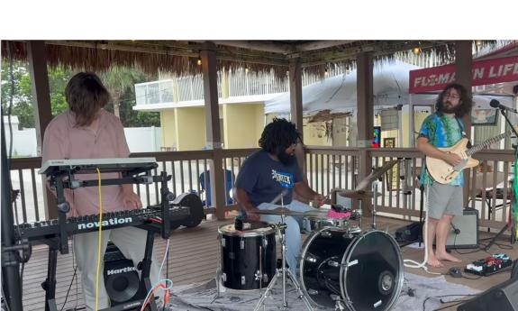 The band Vinegar playing onstage; keyboards, drums, guitar, and vocals.