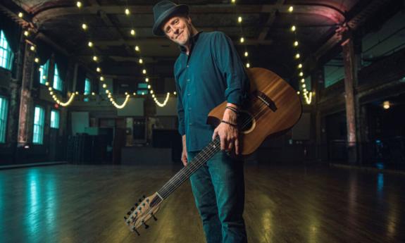 Willy Porter smiles while posing with his guitar.