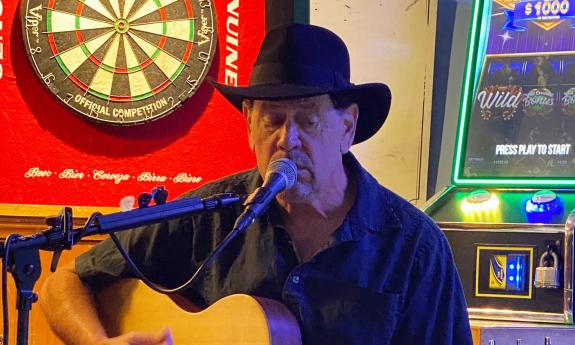 Allen Arena, in a black hat, with his guitar, playing and singing