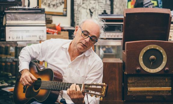 Ed Snodderly playing his guitar among old musical equipment and albums