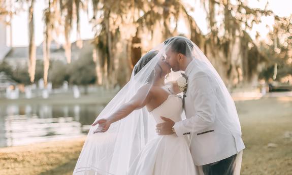Outside The Legacy, a bridal couple kiss under her veil