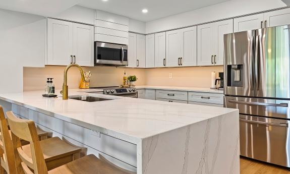 A waterfall eating counter in a white kitchen with stainless appliances
